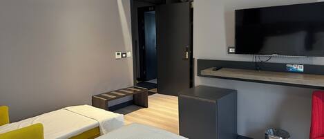 Una camera d'albergo moderna con un letto, una scrivania, una TV e un piccolo angolo relax.