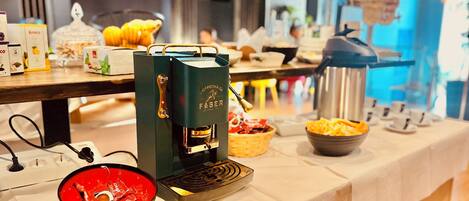Una mesa con una máquina de café, fuentes de aperitivos y un hervidor.