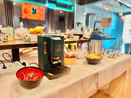 A buffet setup with a coffee machine, bowls of snacks, and a kettle on a table.
