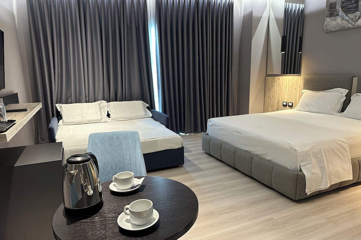 A hotel room with two beds, a desk with a coffee maker, and a table with cups.
