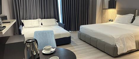 A hotel room with two beds, a desk with a coffee maker, and a table with cups.