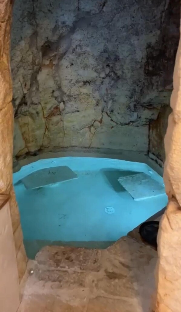 A small, enclosed space with a blue floor, possibly a hot tub or a small pool, surrounded by rough, textured walls. - Carlotta cave a real cave with natural pool (Ostuni)
