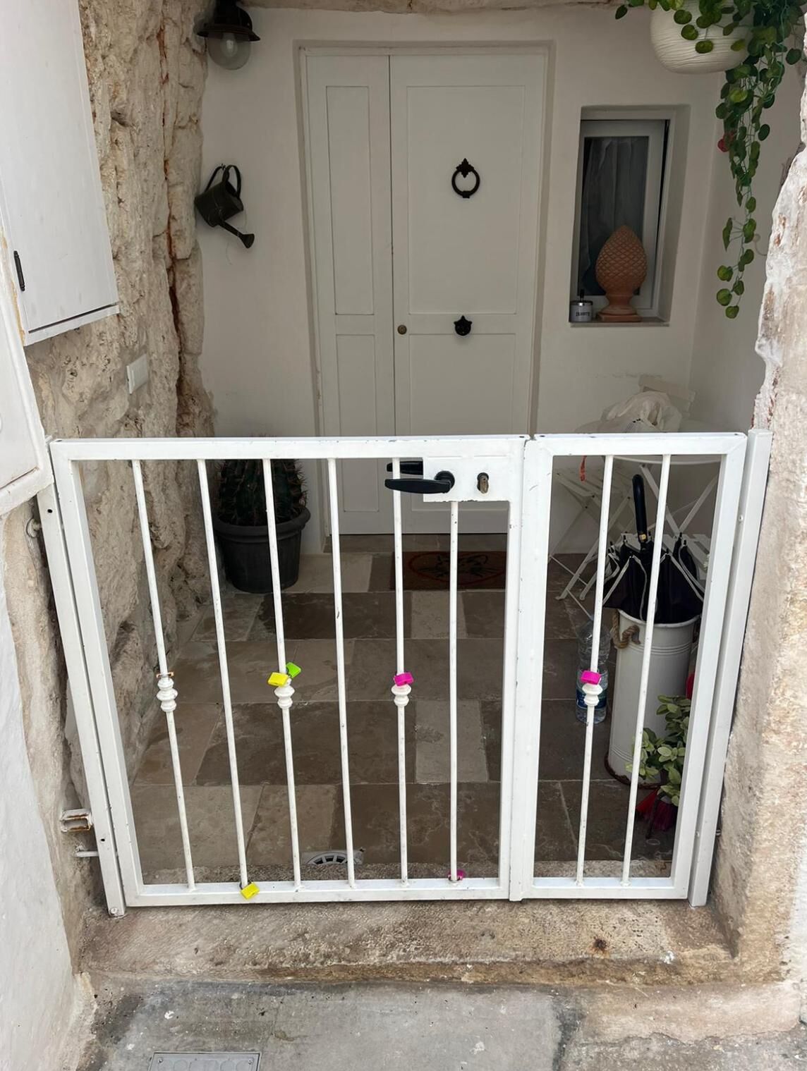 A white metal gate with a handle and a lock, leading to a door with a keyhole and a small window above it.