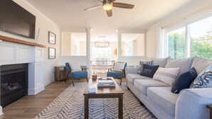 A living room with a fireplace, a ceiling fan, a sofa, and a coffee table. - Tidal Watch 1-Master Suite w/ Ocean View (Kure Beach)