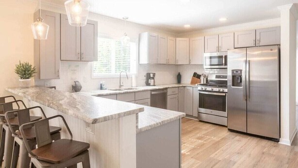 A modern kitchen with a central island, stainless steel appliances, and pendant lighting. - Tidal Watch 1-Master Suite w/ Ocean View (Kure Beach)