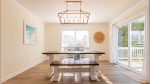 A spacious room with a wooden bench, a hanging light fixture, a large window with blinds, and a view of a balcony. - Tidal Watch 1-Master Suite w/ Ocean View (Kure Beach)