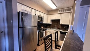 A modern kitchen with stainless steel appliances, white cabinetry, and a central island with bar stools. - Cozy 1-bedroom condo with WiFi in Houston, TX (Houston)