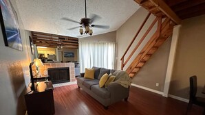 A living room with a fireplace, a sofa, a wooden staircase, and a kitchen in the background. - Cozy 1-bedroom condo with WiFi in Houston, TX (Houston)