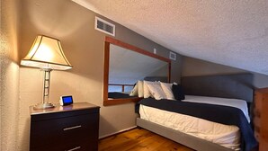 A bedroom with a bed, a bedside table with a lamp, a small desk with a computer, a window with a view, and a wooden floor. - Cozy 1-bedroom condo with WiFi in Houston, TX (Houston)