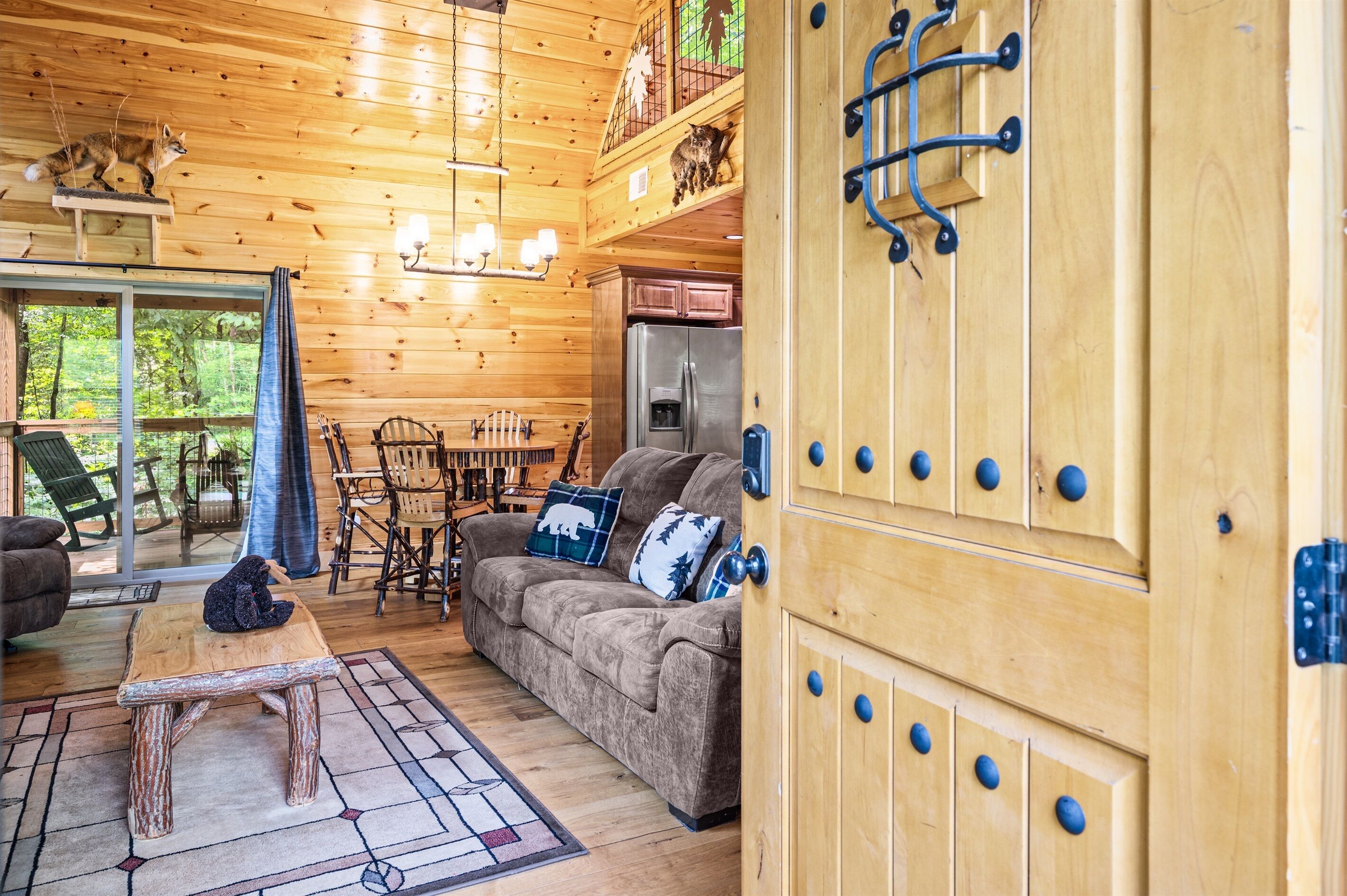 A cozy wooden cabin interior with a sofa, dining table, and a refrigerator.