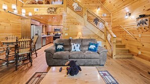 Ein gemütliches Blockhäuschen-Interieur mit einer Holztreppe, einer Couch mit Tierkissen, einem Essbereich und einer Küche.