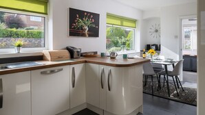 A modern kitchen with white cabinets, a wooden countertop, and a dining area with a table and chairs. - Awel Fryn - Three Bedroom Cottage, Sleeps 6 (Hen Golwyn)