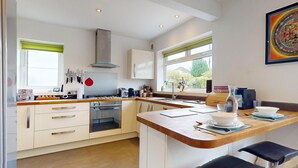 A modern kitchen with white cabinets, a stainless steel range, and a large window. - Awel Fryn - Three Bedroom Cottage, Sleeps 6 (Hen Golwyn)