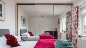 A hotel room with a bed, a mirror, a window with curtains, and a radiator. - Awel Fryn - Three Bedroom Cottage, Sleeps 6 (Hen Golwyn)