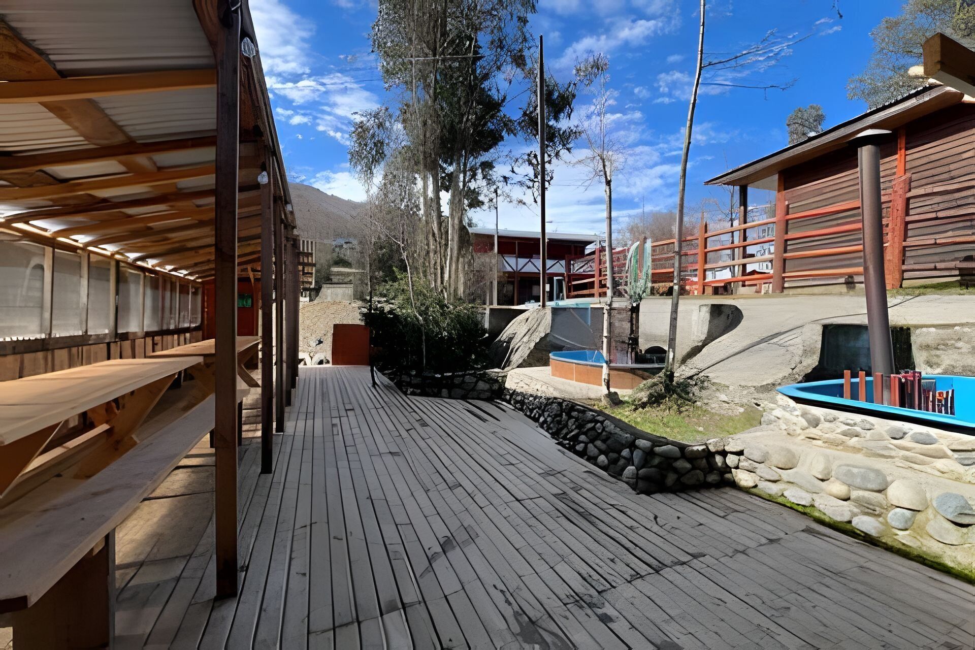 A wooden deck with benches, a stone wall, and a blue pool area.