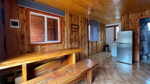 A wooden interior with a wooden bench, a refrigerator, and a window with shutters. - Oceana Suites Rayen Lican-Ray (Villarrica)