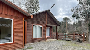 A wooden cabin with a gravel driveway, a fenced area, and a chimney. - Oceana Suites Rayen Lican-Ray (Villarrica)