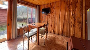 A wooden cabin with a dining table, chairs, a TV mounted on the wall, and a refrigerator. - Oceana Suites Rayen Lican-Ray (Villarrica)