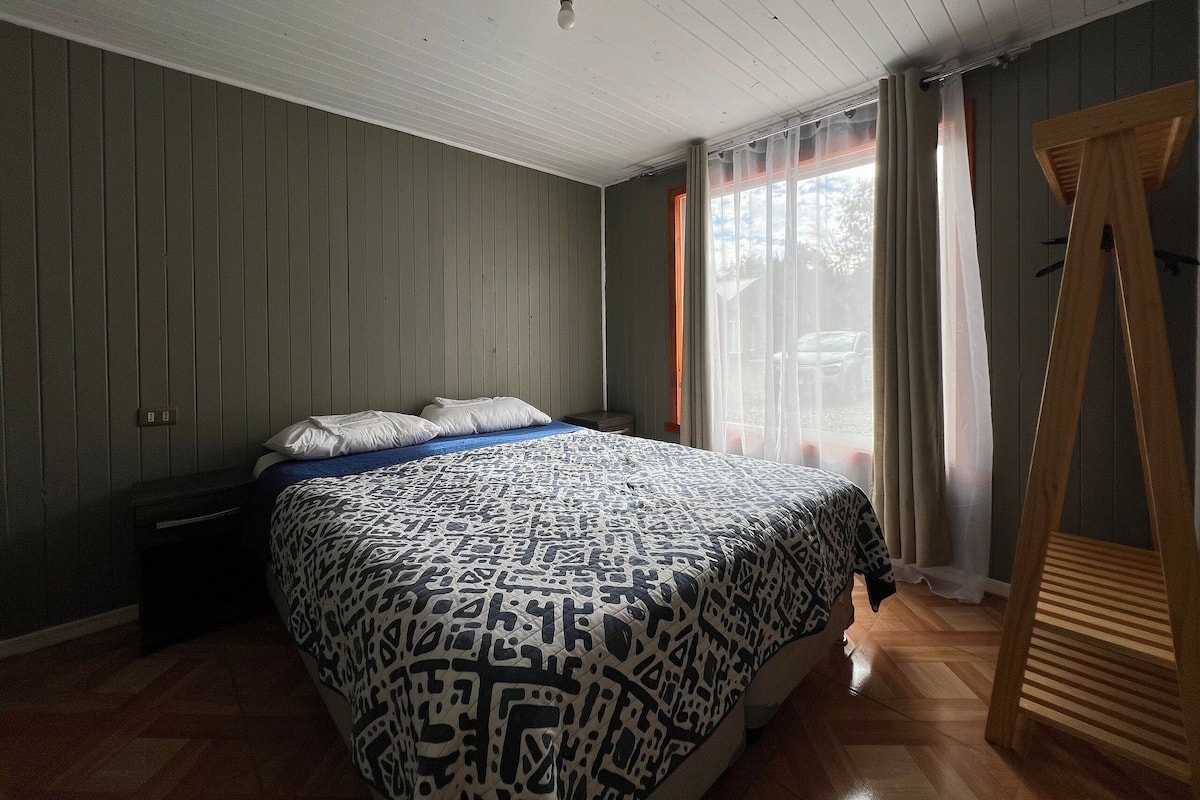 A bedroom with a bed, wooden floor, and a window with curtains.