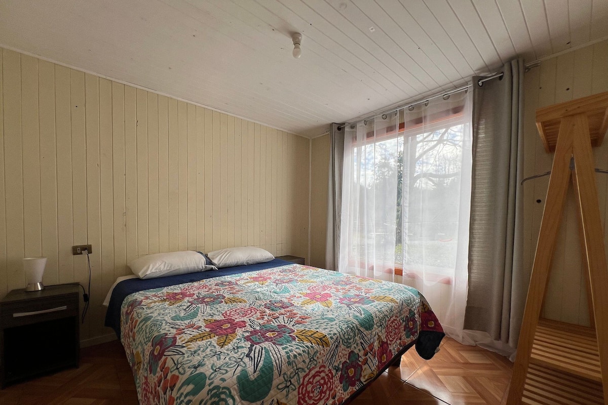 A bedroom with a wooden bed, a nightstand, a lamp, and a window with curtains.