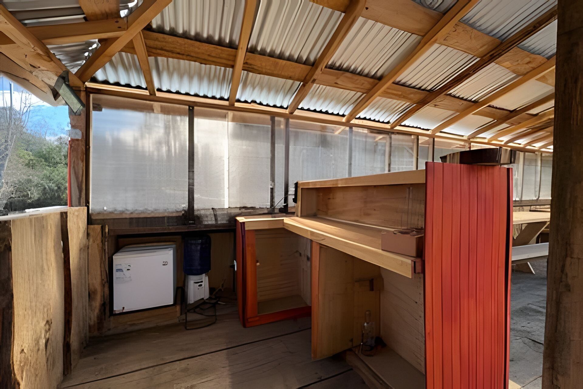 Une structure en bois surmontée d’un toit en métal, avec un établi et un petit réfrigérateur.