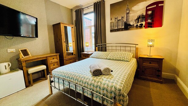 A bedroom with a bed, a desk, a mirror, a TV, and a painting of Big Ben. - Le Papillon Hotel Blackpool (Blackpool)