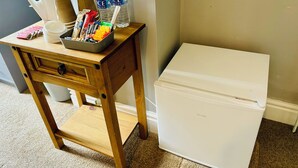 A small wooden table with a kettle, water bottles, snacks, and a coffee maker. A white mini-fridge is next to the table. - Le Papillon Hotel Blackpool (Blackpool)