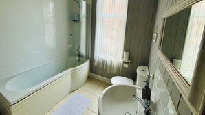 A bathroom with a bathtub, sink, toilet, and a window with curtains. - Le Papillon Hotel Blackpool (Blackpool)