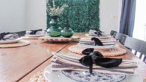 Mesa de jantar posta com pratos, tigelas e guardanapos, com um letreiro de neon ao fundo.