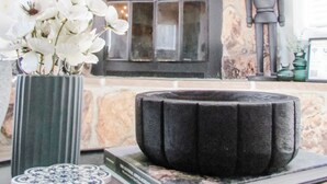 Uma sala de estar moderna com lareira de pedra, uma TV de tela plana acima dela e um vaso decorativo com flores brancas em um console.