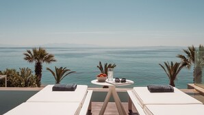 Ein Balkon mit zwei Liegestühlen, einem kleinen Tisch mit einer Obstschale, einem Glas Wasser und Sonnenbrillen.