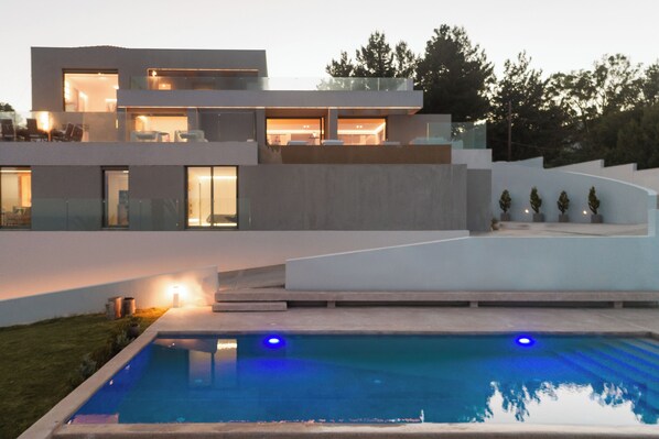 A modern two-story house with a swimming pool, large windows, and a well-lit outdoor area.