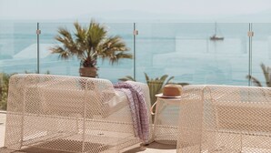 Ein Balkon mit zwei Korbstühlen, einem kleinen Tisch und einer Blumentopf-Pflanze.