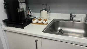 Keittiössä on kahvinkeitin, vedenkeitin ja kolme pientä astiaa työtasolla.
