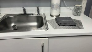 Keittiössä on ruostumattomasta teräksestä valmistettu pesuallas, paperipyyhkeiden pidike ja lasinen säilytysastia työtasolla.