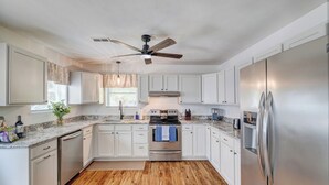 A modern kitchen with white cabinets, stainless steel appliances, and a wooden floor. - Spacious 3bd Home~10min IU Baseball~2 K Beds~Huge Kitchen~Fire Pit+Ping Pong (Bloomington)