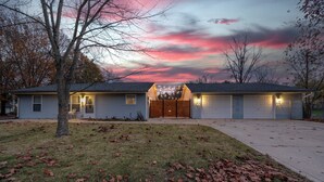 A two-story house with a garage, a front yard with fallen leaves, and a tree. - Spacious 3bd Home~10min IU Baseball~2 K Beds~Huge Kitchen~Fire Pit+Ping Pong (Bloomington)