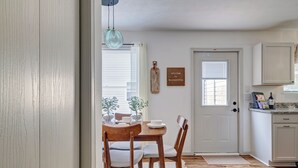 A dining area with a wooden table and chairs, a white door, and a kitchen area with cabinets and a countertop. - Spacious 3bd Home~10min IU Baseball~2 K Beds~Huge Kitchen~Fire Pit+Ping Pong (Bloomington)