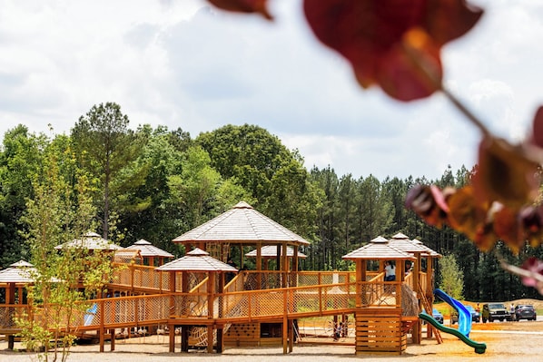 Un terrain de jeux doté de structures en bois, notamment d’un toboggan et d’aires d’escalade, le tout entouré d’arbres.