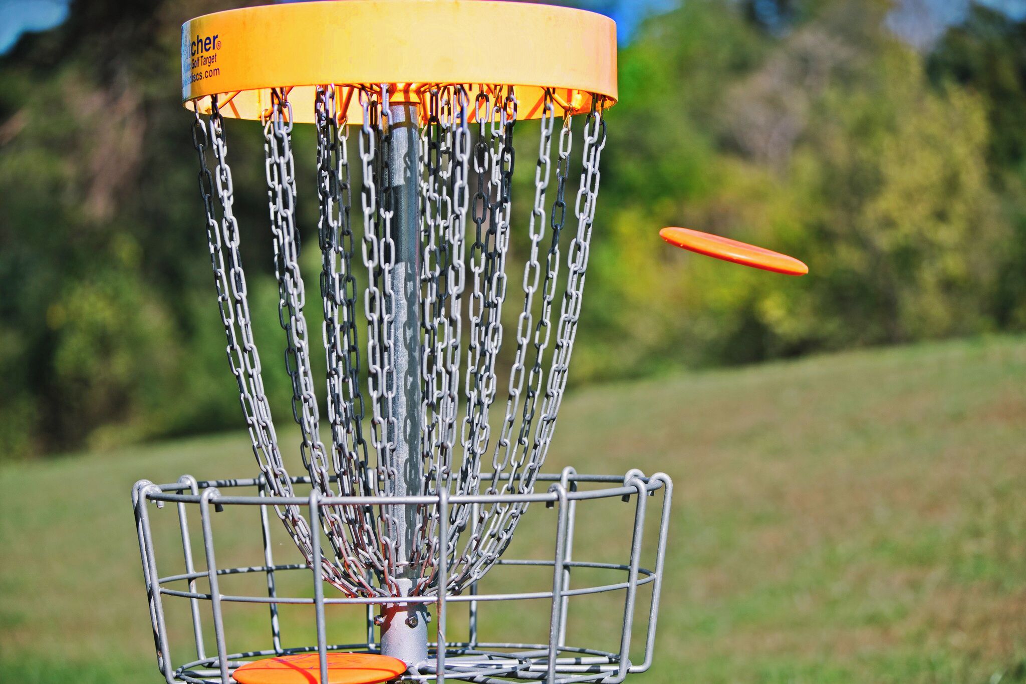 A metal disc golf basket with chains and a yellow top.