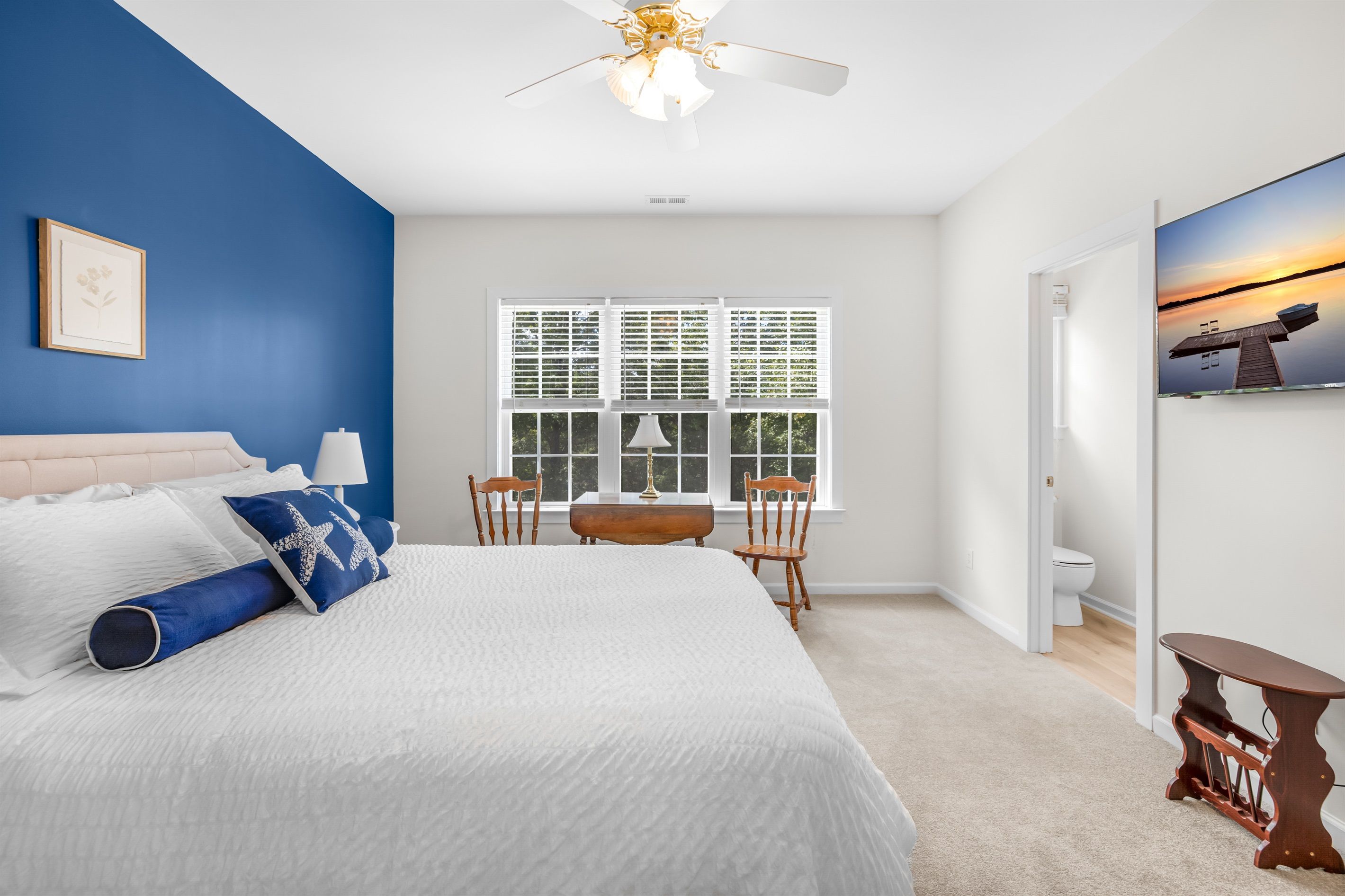 Upstairs primary bedroom with a blue accent wall, ceiling fan and TV.