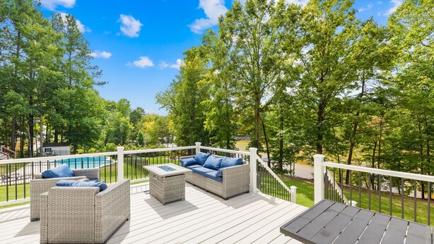 A deck with wicker furniture and a pool in the background.