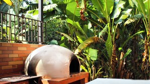 A brick oven pizza oven in a garden setting with lush banana plants and a brick wall. - Finca Hotel Villa Gladys (El Colegio)