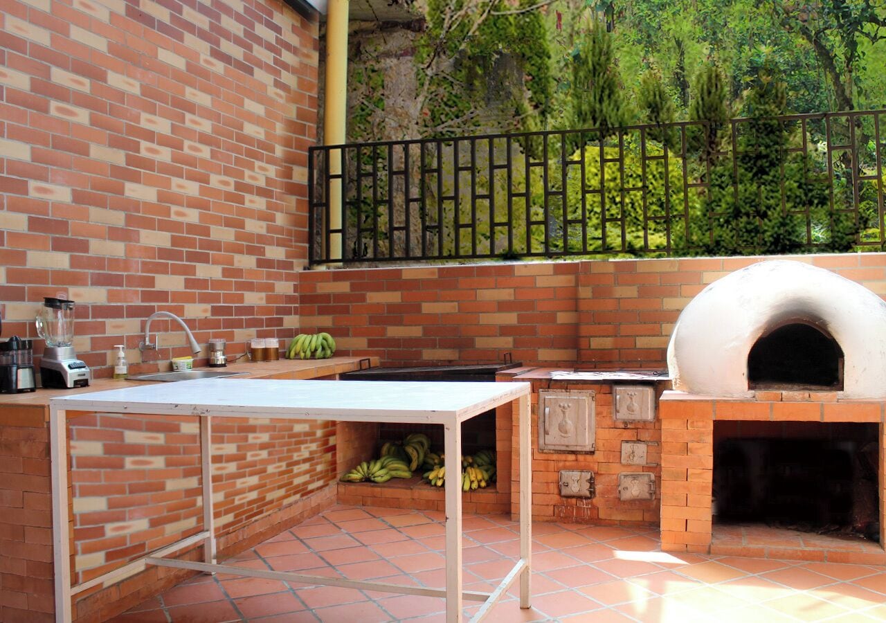 An outdoor kitchen with a brick wall, a metal fence, and a brick oven.