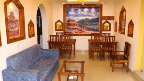 A living room with a blue sofa, wooden chairs, a glass coffee table, and framed pictures on the walls. - Thani Boutique Hotel (Kathmandu)