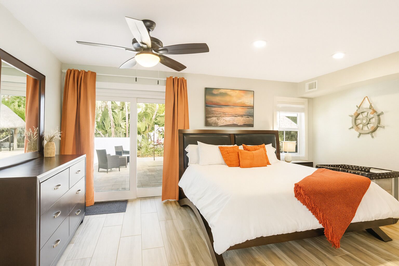 A bedroom with a bed, a ceiling fan, a nightstand, a desk, and a view of the outdoors.