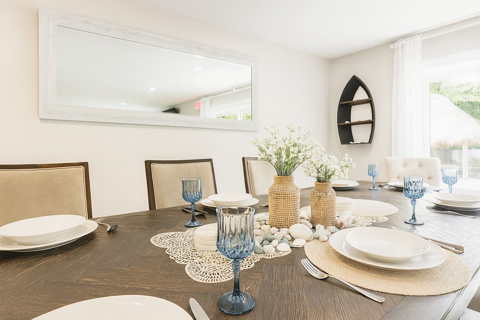 Une table à manger dressée avec des assiettes, des couverts et des objets décoratifs, avec un miroir et une fenêtre en arrière-plan.