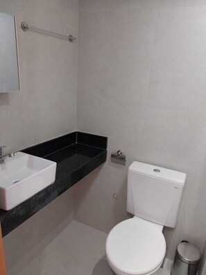 A compact bathroom with a white toilet, sink, and towel rack, set against a light-colored backdrop.