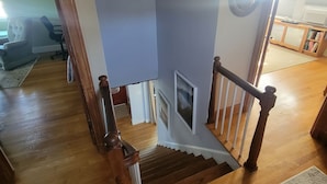 A wooden staircase with a handrail, leading to a landing with a view of a room with a window and a door. - Experience Classic Charm in a Cozy 115-Year-Old Colonial (Waltham)