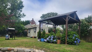 A stone wall, a covered patio, and a house with a chimney. - Experience Classic Charm in a Cozy 115-Year-Old Colonial (Waltham)